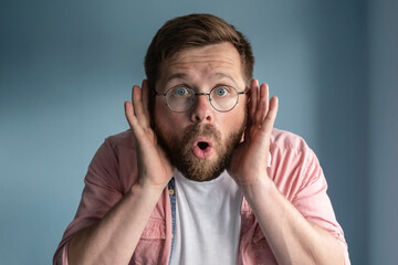 Man with glasses eavesdrops with his hands to ears, he opened mouth in shock and looks with big...