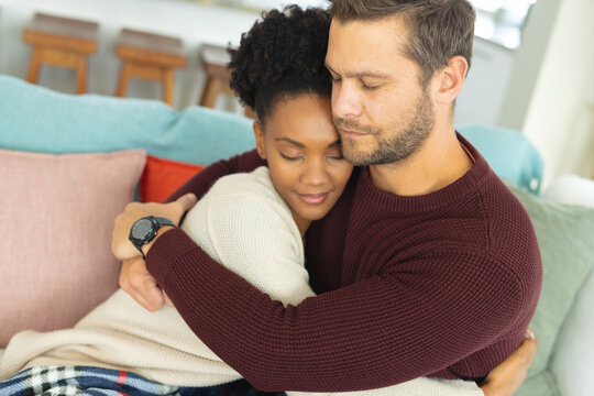Image of diverse couple embracing on sofa