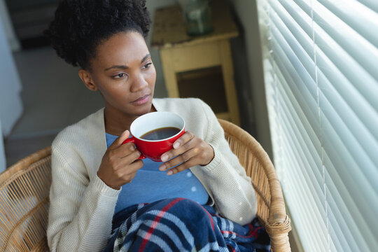 Image of thoughtful african american woman with coffee looking outside window