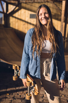 Vertical image of happy caucasian woman holding skateboard in skate shop