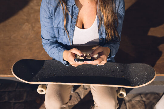 Image of midsection of caucasian woman with smartphone resting in skate park