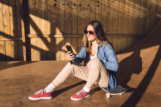 Image of relaxed caucasian woman with smartphone resting in skate park