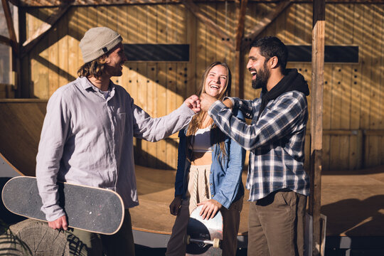 Image of happy diverse female and male friends with skateboards in skate park