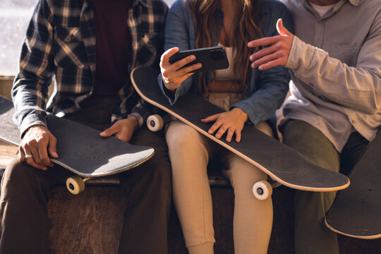 Image of midsection of diverse female and male friends with smartphone in skate park