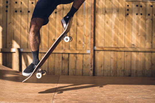 Image of low section of caucasian man jumping on skateboard in skate park