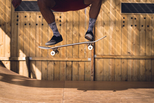 Image of low section of caucasian man jumping on skateboard in skate park