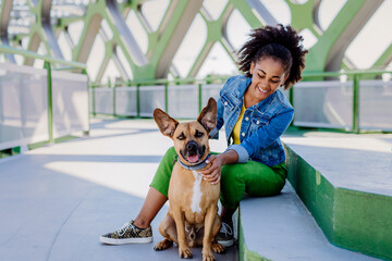 Multiracial girl sitting and resting with her dog outside in the bridge, training him, spending leisure time together. Concept of relationship between dog and teenager, everyday life with pet.