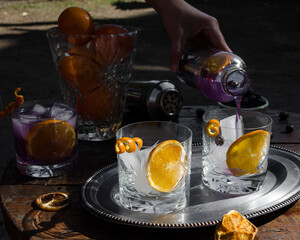 Woman hand serving refreshing purple drink with ice and orange slice. Concept of the drink