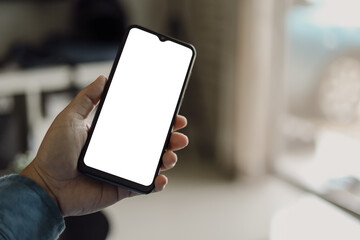 Mockup image of a man holding black mobile phone with blank white screen. In living room at home.