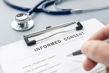 Hand filling a Informed Consent form and stethoscope on desk