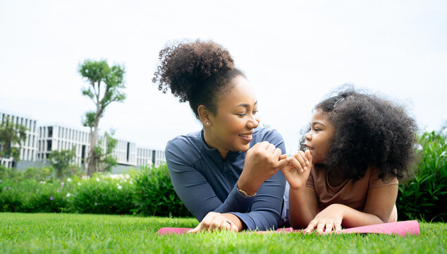 Happy african american mother and daughter in sportswear cuddling while exercising together outdoor , cute teen girl kissing her pretty mom laying on yoga mat, city park,out door,  copy space