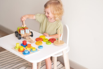 Obraz na płótnie Canvas Happy laughing toddler, baby girl playing with colourful wooden eco-friendly toys,construct.Child Montessori activity, game.Early kid development, lifestyle copy space.