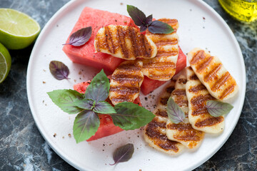 White plate with watermelon, grilled haloumi cheese and fresh basil, middle close-up, elevated view