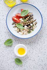 Plate with grilled eggplant and goat cheese salad, top view on a light-grey granite background, vertical shot with space