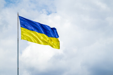 A damaged flag of Ukraine flies against the background of a cloudy sky.