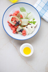Plate with watermelon, cucumber and cheese salad, above view on a light-beige stone background, vertical shot with space