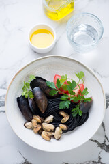 Plate with squid-ink spaghetti, mussels and parsley on a white marble background, studio shot, selective focus