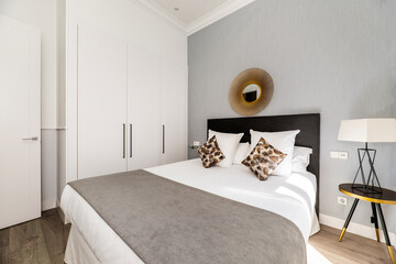 Bedroom with double bed with brown upholstered fabric headboard, matching cushions and built-in wardrobe with white doors