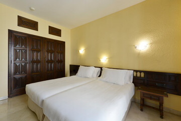 Bedroom with a double bed with a long dark wood headboard, matching side tables and a built-in wardrobe with vintage wooden doors