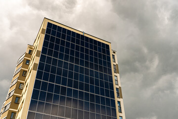 A modern energy-efficient building against the background of clouds. Multi-storey residential building with solar panels on the wall. Renewable energy sources in the city