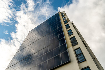A modern energy-efficient building against the background of clouds. Multi-storey residential building with solar panels on the wall. Renewable energy sources in the city