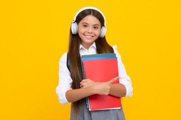 Teenage student, school girl with books and headphones listening to music on yellow background. Happy schoolgirl.