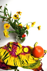 still life with orange pumpkin, yellow squash and garden flowers boquete in vase on bright textile  background