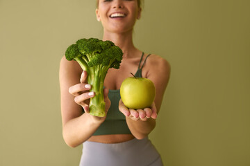  Cropped image of girl holding broccoli and green apple on green background.