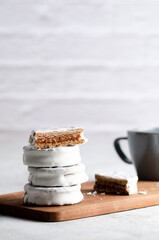 White alfajores filled with dulce de leche and a blue cup on a wooden board and white background. 