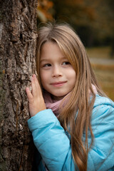 portrait of beautiful girl with long blonde hair staying near tree  in autumn park