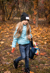 child with long hair in black hat in autumn forest with bag