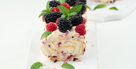Baked meringue roll with cream and fresh fruits on a white wooden board, delicious dessert