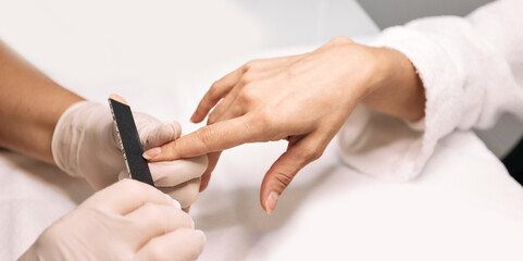 Manicurist filing woman's nails at her working table. Nail care process, close-up