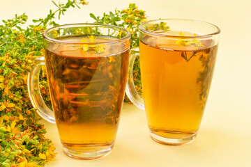 Two transparent mugs with tea (decoction, infusion) from the medicinal herb St. John's wort on a yellow background. Alternative medicine, herbs for health, herbal medicine.