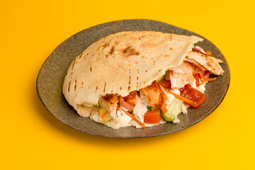 Shawarma in a pit with vegetables and chicken, side view yellow background