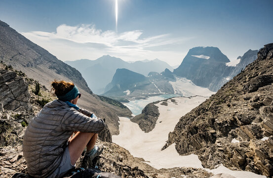 Woman In Puffy Coat Looks Out Over Grinnell Glacier On Smoky Day