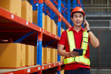 factory worker or warehouser holding a tablet and talking on smartphone in the warehouse storage