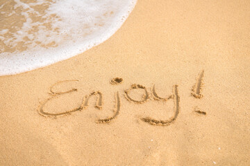 The handwritten word enjoy on the golden sand, vacation and happiness concept