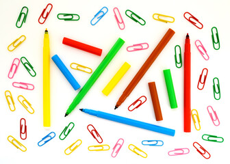 school background wallpaper with paper clips and colored felt-tip pens close-up on a white background for design