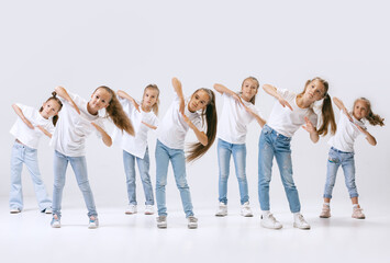 Obraz premium Dance group of happy, active little girls in jeans and t-shirts dancing isolated on white studio background. Concept of music, fashion, art, childhood, hobby