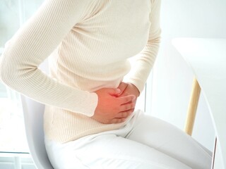 Young woman sitting in a chair at home and suffering from colics. Closeup photo, blurred.