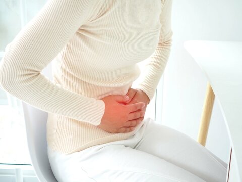 Young woman sitting in a chair at home and suffering from colics. Closeup photo, blurred.