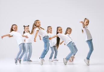 Dance group of happy, active little girls in jeans and t-shirts dancing isolated on white studio...
