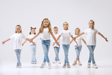 Dance group of happy, active little girls in jeans and t-shirts dancing isolated on white studio background. Concept of music, fashion, art, childhood, hobby