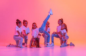 Group of children, school age girls in sportive casual style clothes dancing in choreography class isolated on pink background in yellow neon light.
