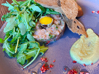 Raw salmon tartare with quail egg and fresh arugula  closeup. Healthy food concept.