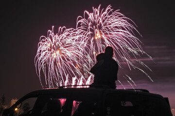 silhouette of a family watching fireworks on the roof of their car - obrazy, fototapety, plakaty