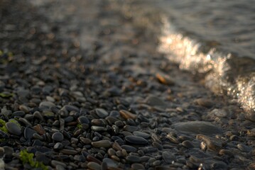 A transparent sea wave rolls over a rocky beach, the concept of rest and travel, calmness and reflection on a warm summer day, defocusing, blurred background, selective focus, bokeh.