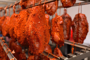 mouth-watering pieces of pork delicacies in paprika and seasonings are hung on a metal rack in a meat-packing plant or butcher's shop.