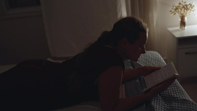 At night, the girl lies on the edge of the bed, and flips through a notebook. View from above